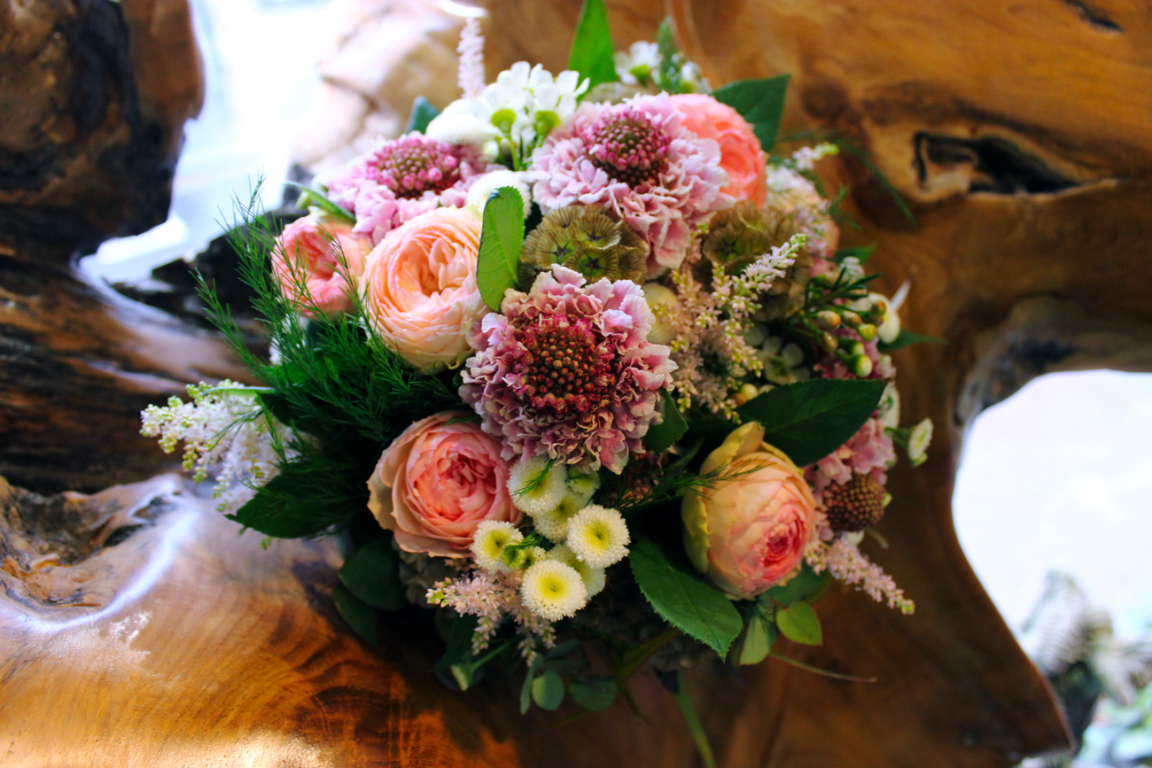 Bouquet de mariée posé sur une souche d’arbre exotique. Le bouquet
contient des scabieuses, des roses, des matricaires et de l’astilbe.